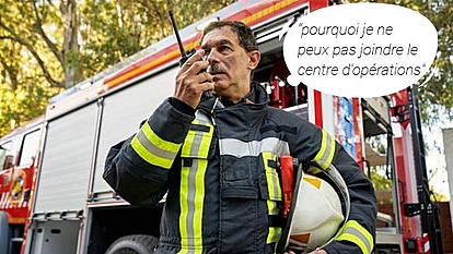 Réseau de communication critique – Assurer une réponse d’urgence fiable Pompier utilisant une radio devant un camion de pompiers et rencontrant des difficultés pour joindre le centre d’opérations. Représente l’importance des réseaux de communication critiques fiables.