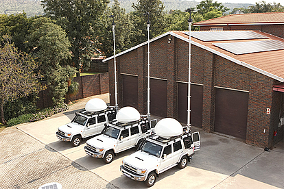 Vehicle-Based Monitoring Units for Mobile Spectrum Analysis Four white monitoring vehicles equipped with antennas parked outside a brick building, representing LS telcom’s mobile spectrum monitoring solutions for flexible deployment.