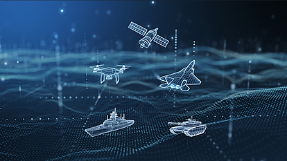 Digital hologram visualization of military assets including satellite, drone, fighter jet, naval ship, and tank over a data network background, representing defense communication and spectrum management technology.