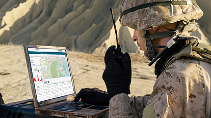 Soldier using a laptop in the field for automated spectrum management and defense mission planning.
