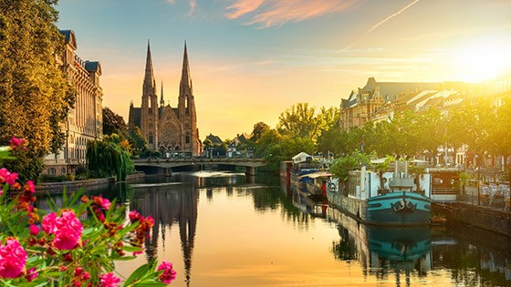 Strasbourg canals, historic church, and buildings at sunset with vibrant flowers.